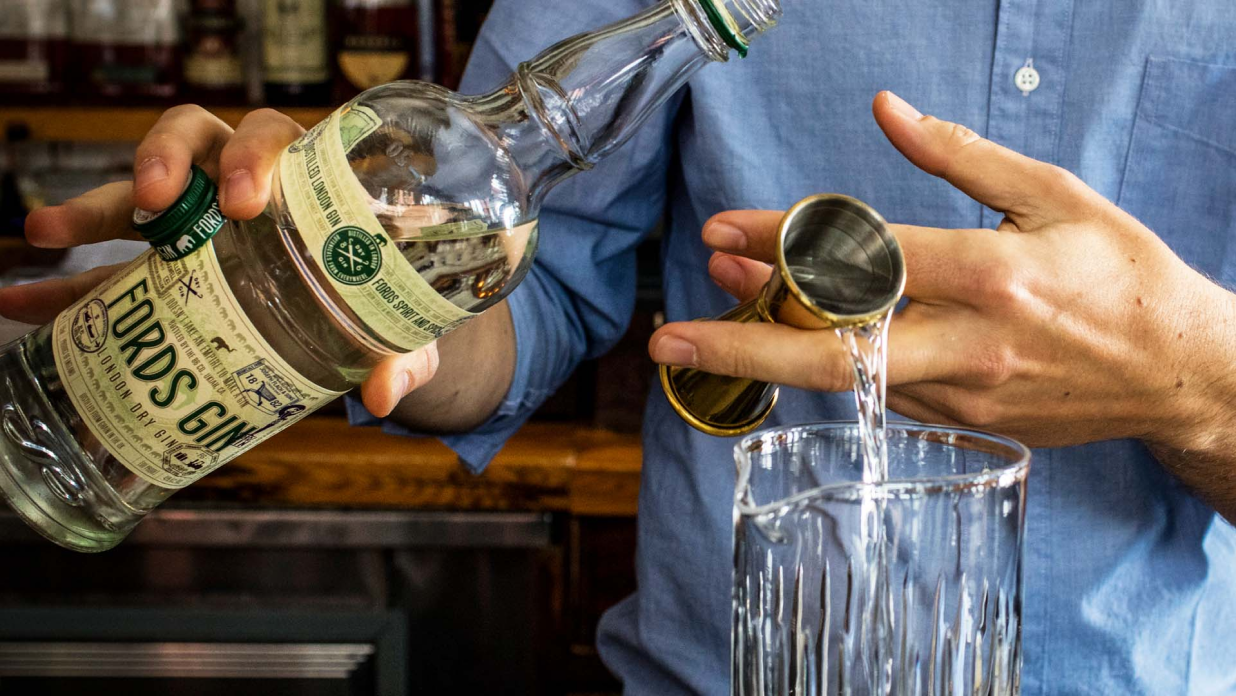 Bartender pouring from a Fords Gin bottle into a mixing glass.